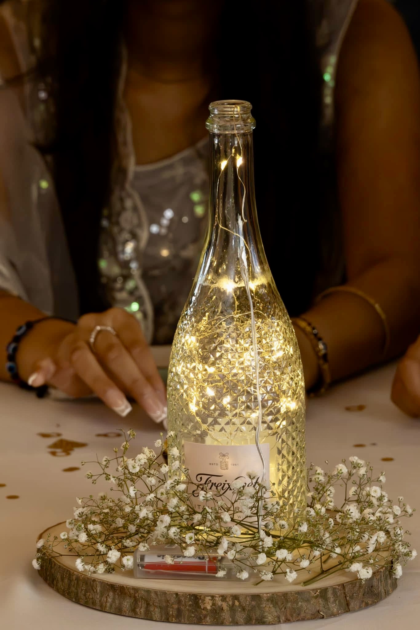 Bottle lit with fairy lights on a flower-scattered table