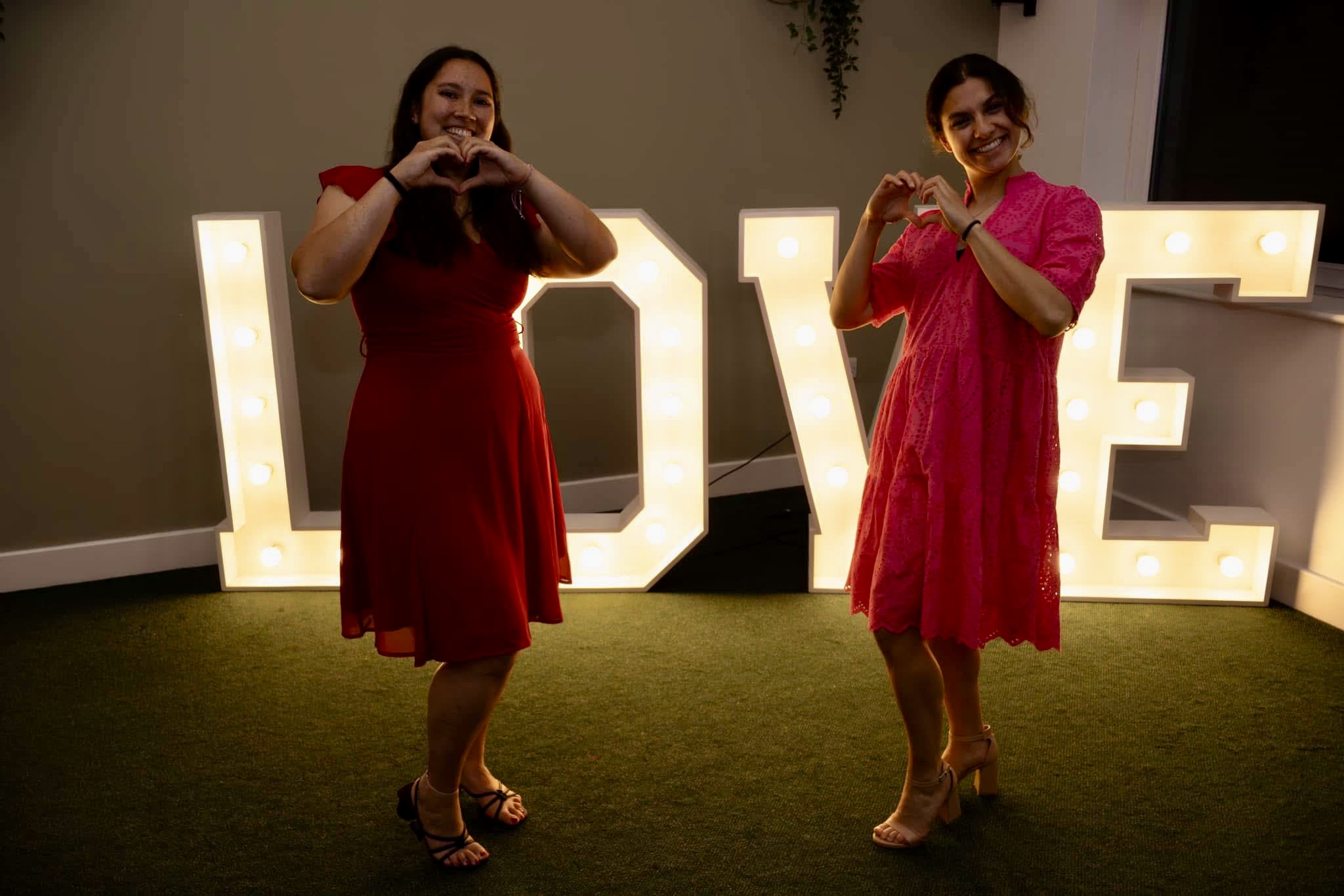 Two guests in dresses making hearts in front of LOVE light-up letters