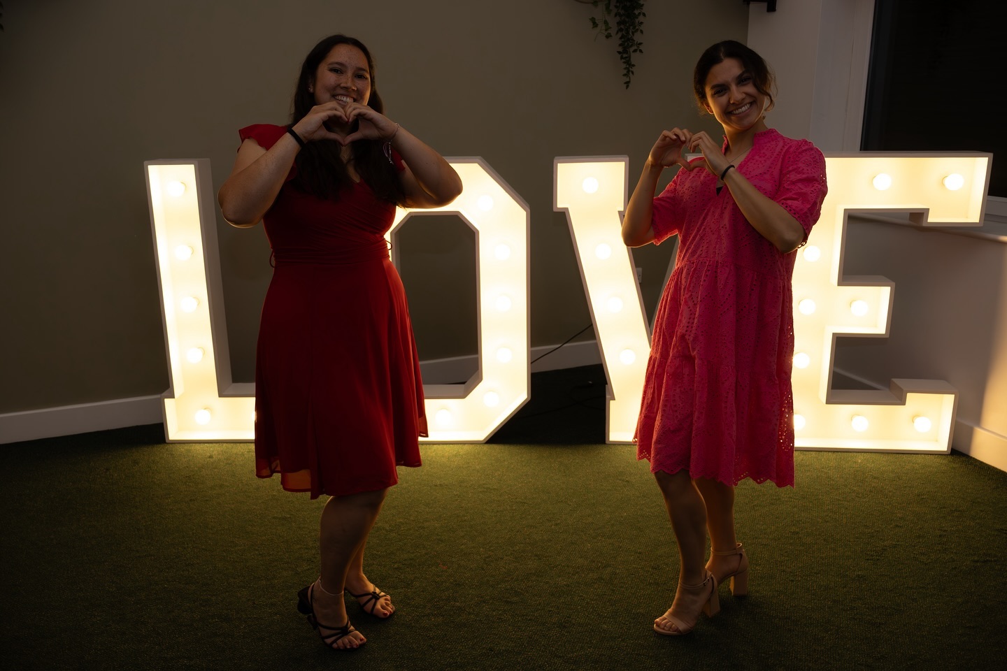 Two guests in red dresses in front of LOVE light-up letters